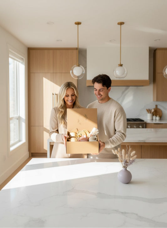 A smiling couple holding a Kintoir Cozy Mornings coffee gift box in a bright, modern kitchen.