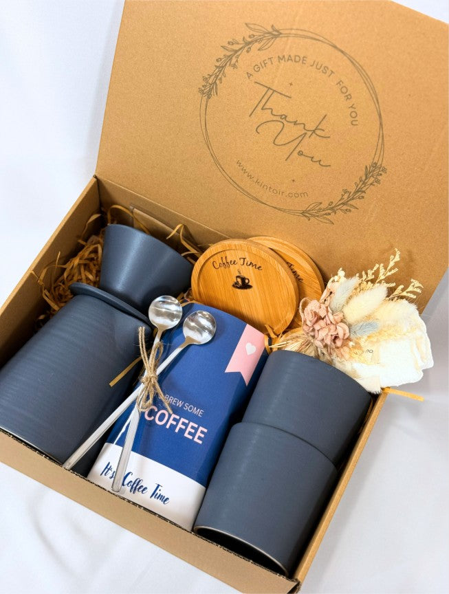 Kintoir coffee gift box featuring a pour-over maker, two grey ceramic mugs, spoons, coasters, and dried flowers.