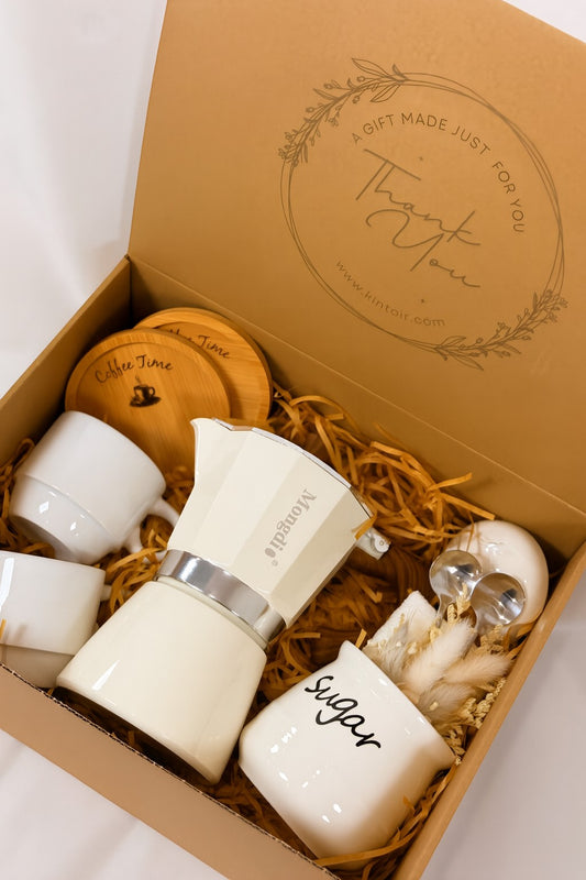 Kintoir luxury espresso gift box featuring a cream stovetop coffee maker, two white mugs, sugar bowl, and wood coasters.