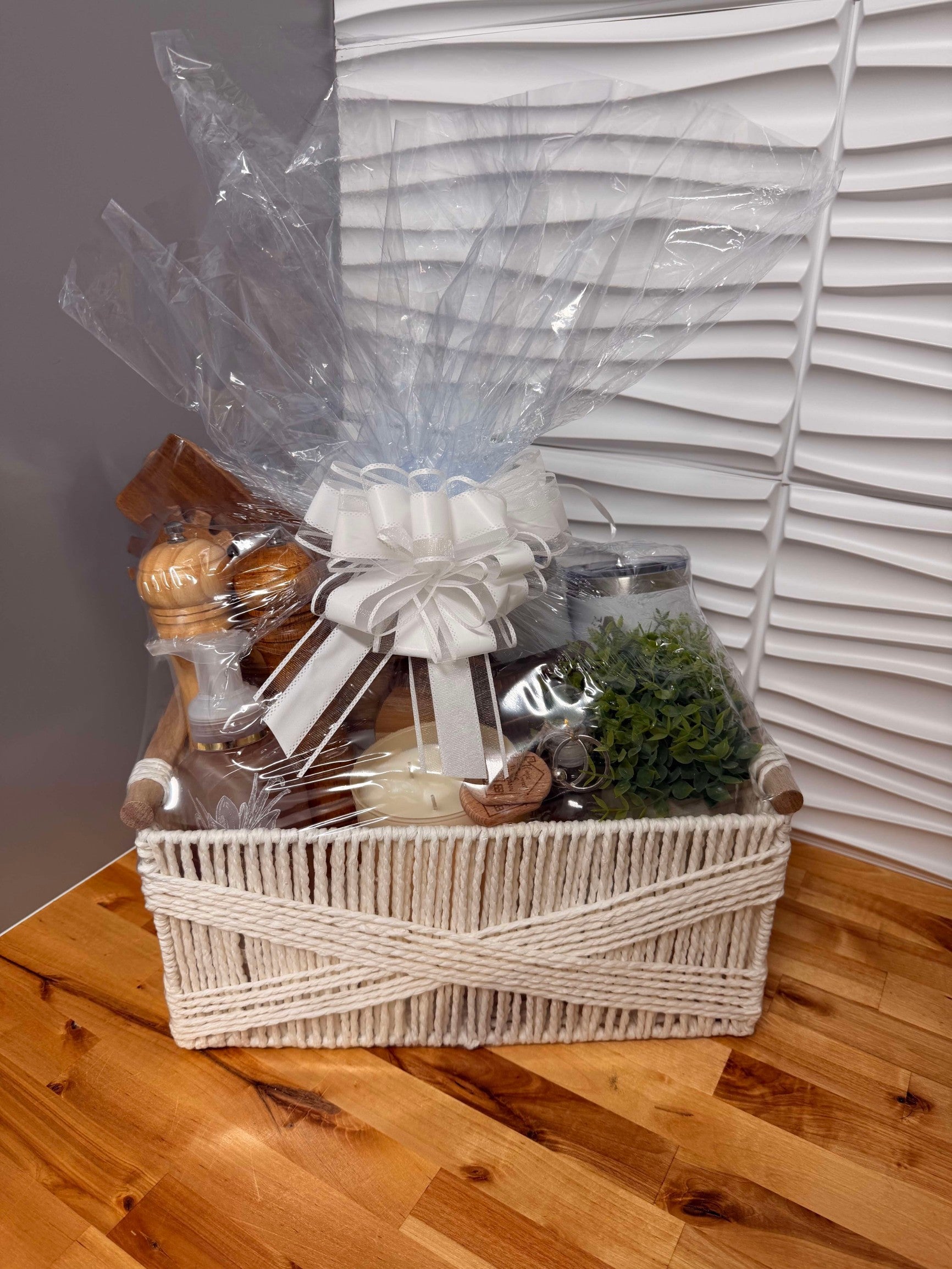 Kintoir gift basket featuring a white rope container, wooden kitchen tools, faux plant, and candle with a white bow.