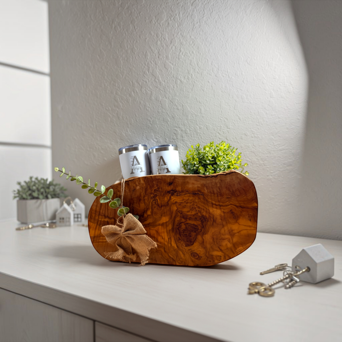 Olive wood serving board styled with greenery and white tumblers from the Grand Welcome closing gift basket